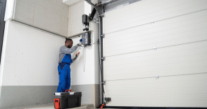 A technician in blue overalls repairs a garage opener.